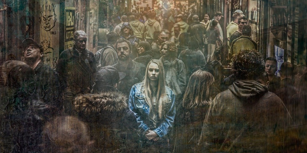 A girl standing in middle of people glued to their phones.